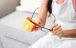 Person cleaning eyeglasses with microfiber cloth and lens-safe spray