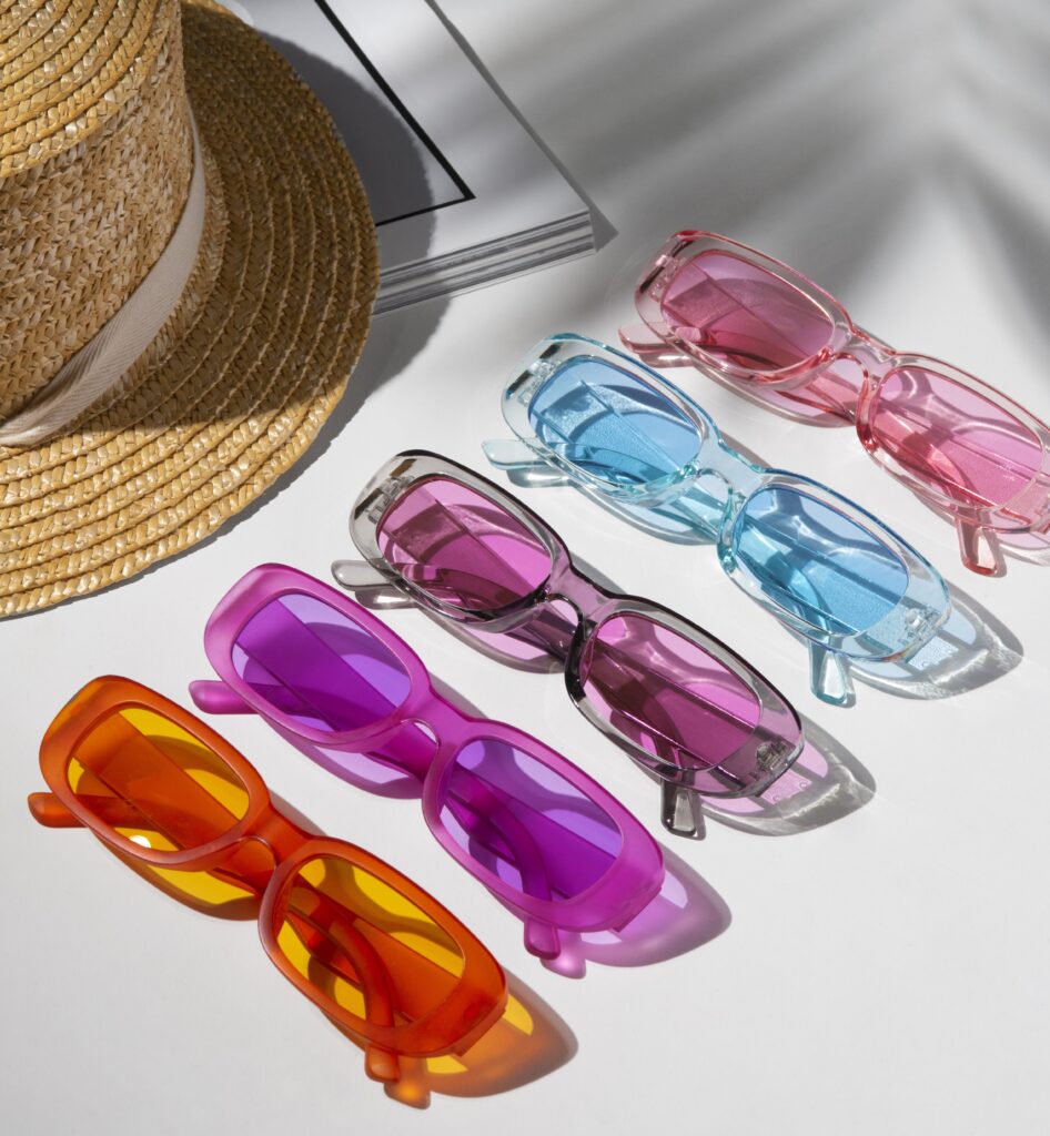 Colorful transparent sunglasses on white background with summer hat, representing frame color choices